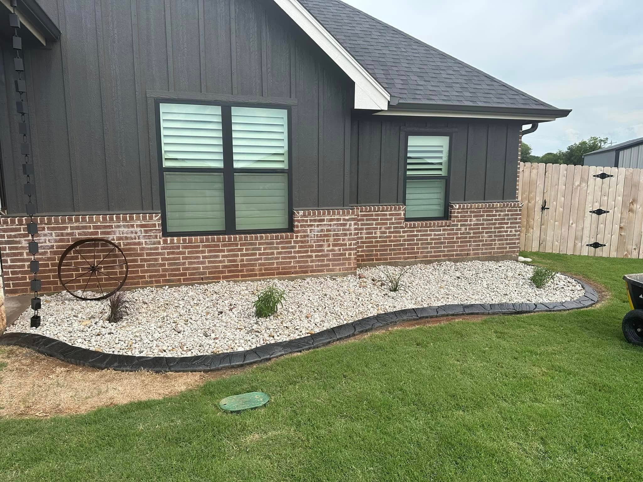 Finished curved river-rock landscape bed beside a dark home
