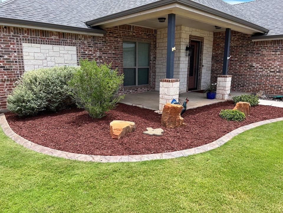 Finished curved front landscape bed with red mulch and young plants